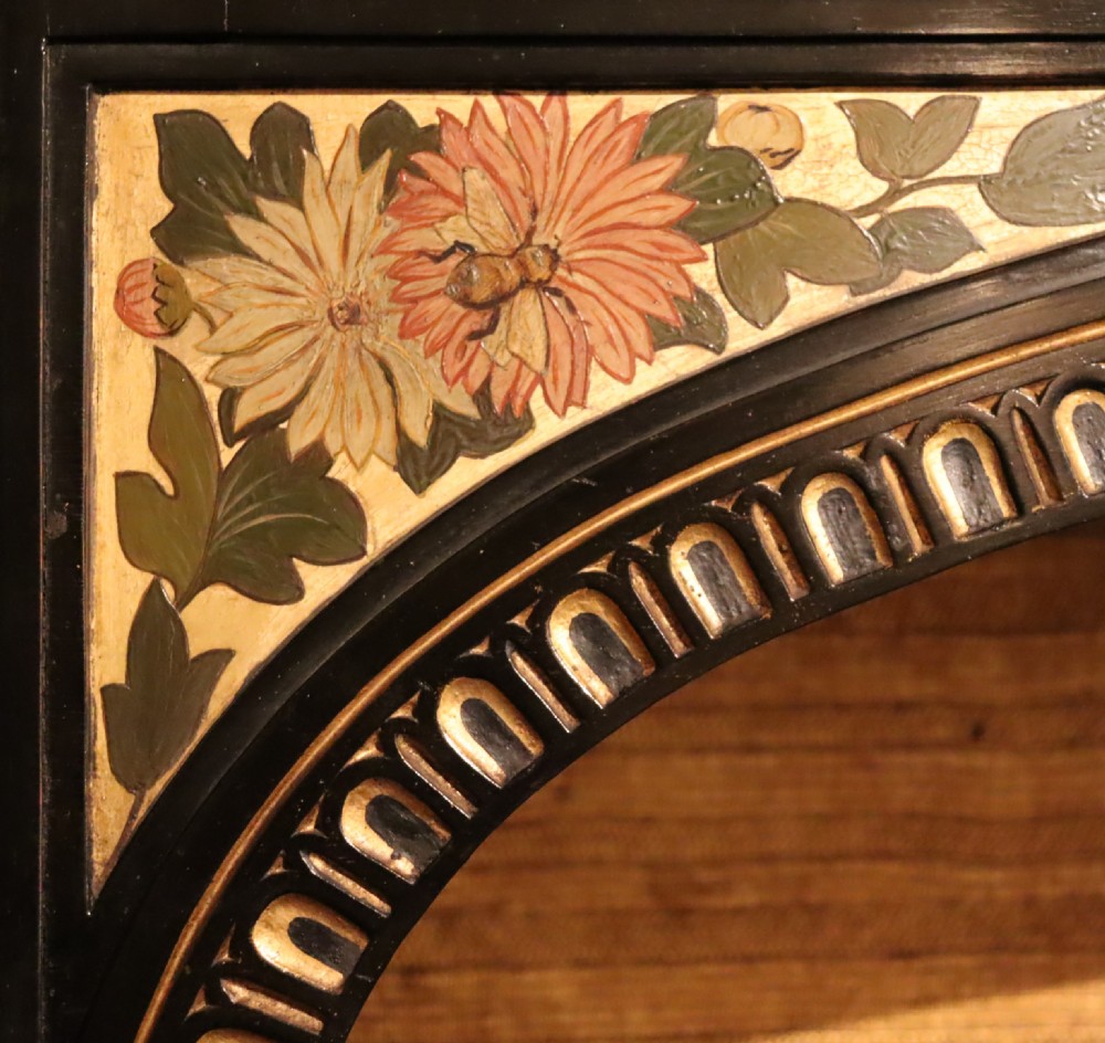 An Aesthetic Movement ebonised mahogany display cabinet featuring gilt highlights, turned spindle arcades, painted floral panels, and mirrored doors. View VI
