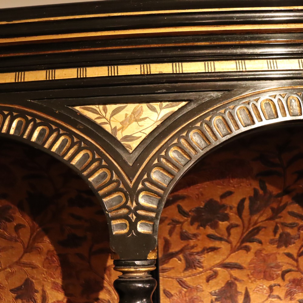An Aesthetic Movement ebonised mahogany display cabinet featuring gilt highlights, turned spindle arcades, painted floral panels, and mirrored doors. View VIII