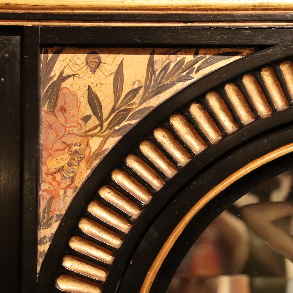 An Aesthetic Movement ebonised mahogany display cabinet featuring gilt highlights, turned spindle arcades, painted floral panels, and mirrored doors. View IX