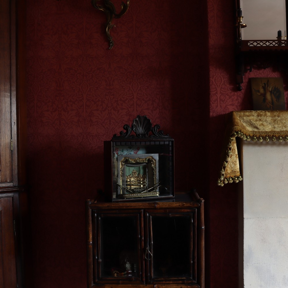 A Victorian miniature fireplace model with brass and iron hearth details, enclosed in a dark wood cabinet with a shell carved pediment. View III