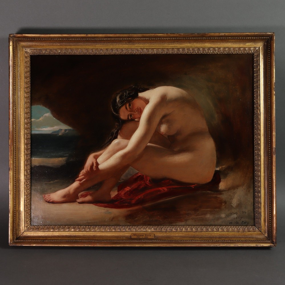 An antique oil painting on wood panel depicting a seated female nude inside a dark cave facing a seascape, set within a gilded molded frame.