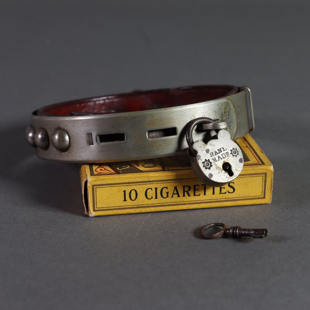 An Edwardian white metal dog collar featuring a brown leather lining, raised metal studs, an attached brass bell, and a functional padlock with key. View V