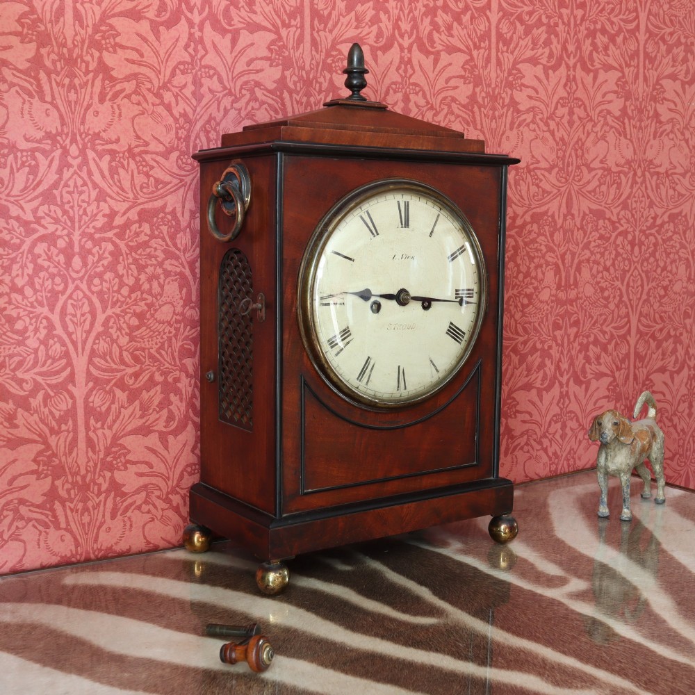 A George IV mahogany bracket clock featuring ebony inlaid lines, brass ball feet, side carrying handles, and a circular white dial signed by L. Vick of Stroud. View II