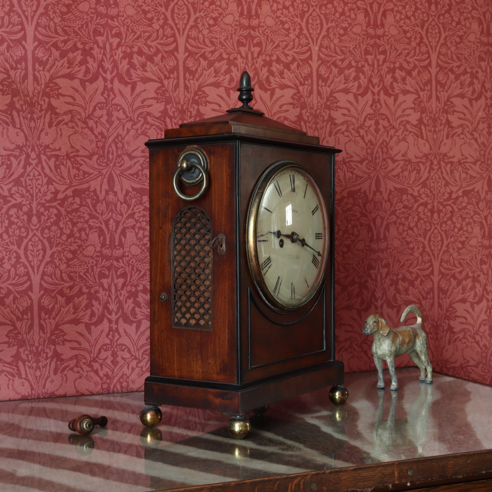 A George IV mahogany bracket clock featuring ebony inlaid lines, brass ball feet, side carrying handles, and a circular white dial signed by L. Vick of Stroud. View III