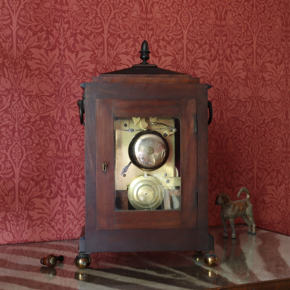 A George IV mahogany bracket clock featuring ebony inlaid lines, brass ball feet, side carrying handles, and a circular white dial signed by L. Vick of Stroud. View V