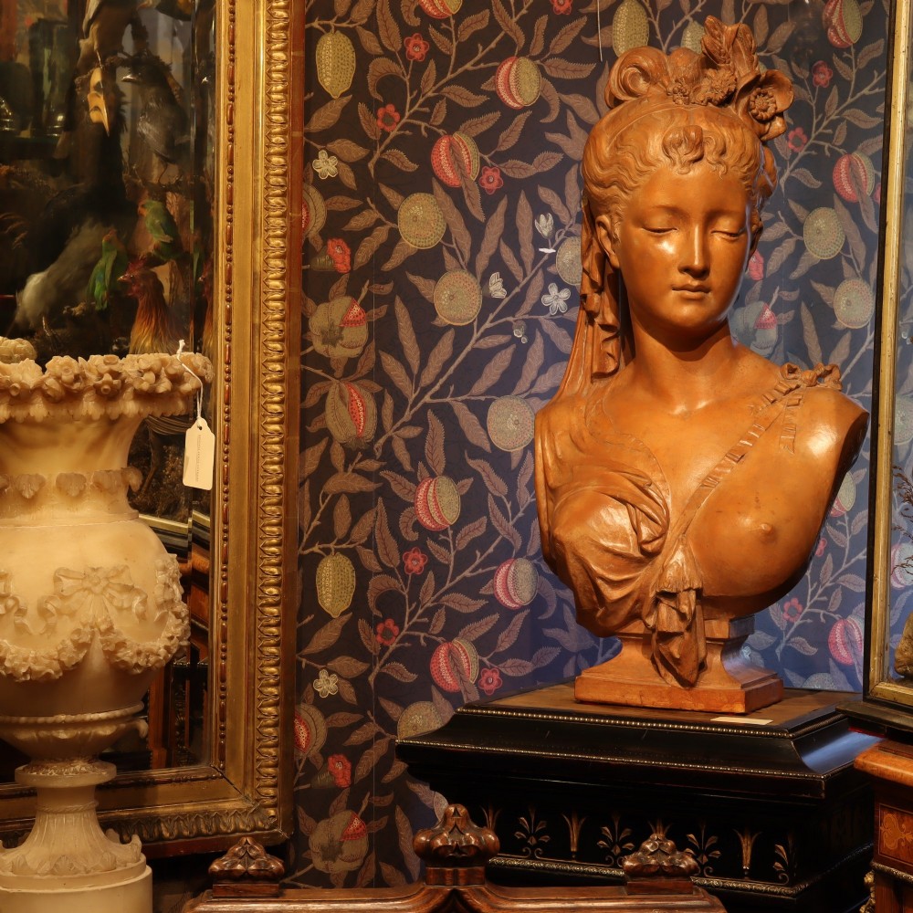 A Neoclassical terracotta bust depicting a young woman with a floral hair arrangement and draped semi-nude torso set on an integrated base. View II