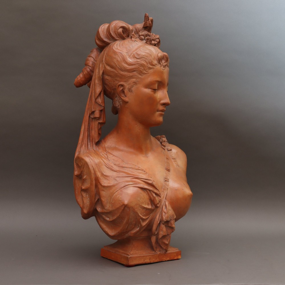 A Neoclassical terracotta bust depicting a young woman with a floral hair arrangement and draped semi-nude torso set on an integrated base. View VI
