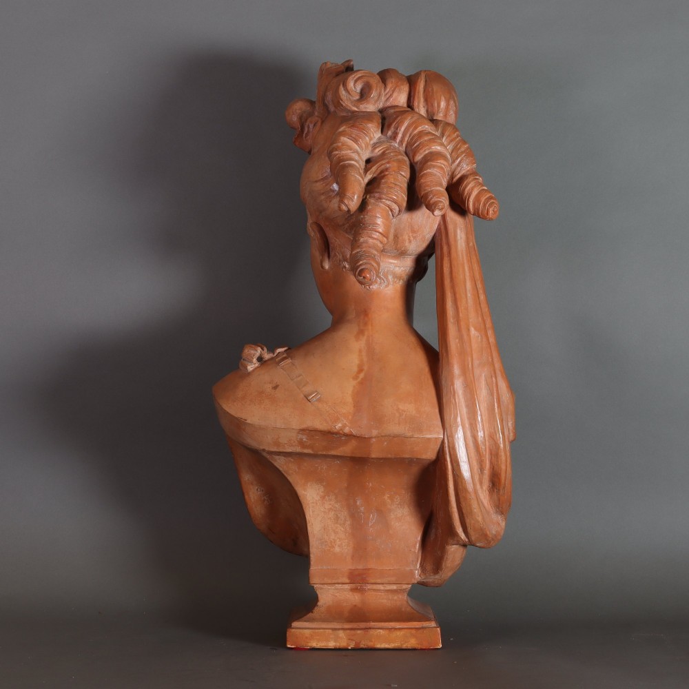 A Neoclassical terracotta bust depicting a young woman with a floral hair arrangement and draped semi-nude torso set on an integrated base. View IX