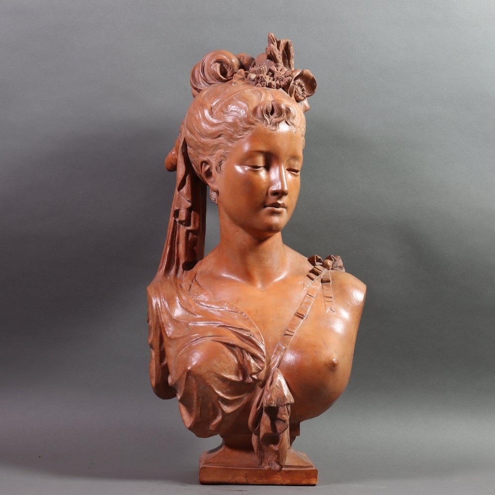 A Neoclassical terracotta bust depicting a young woman with a floral hair arrangement and draped semi-nude torso set on an integrated base. View X