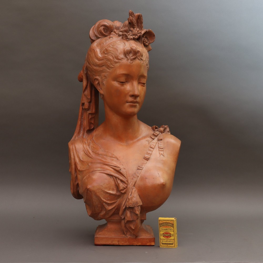 A Neoclassical terracotta bust depicting a young woman with a floral hair arrangement and draped semi-nude torso set on an integrated base. View XI