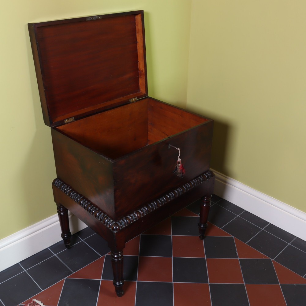 A Georgian flame mahogany rectangular cellarette chest on a stand featuring turned legs, gadrooned trim, and brass castors. View II