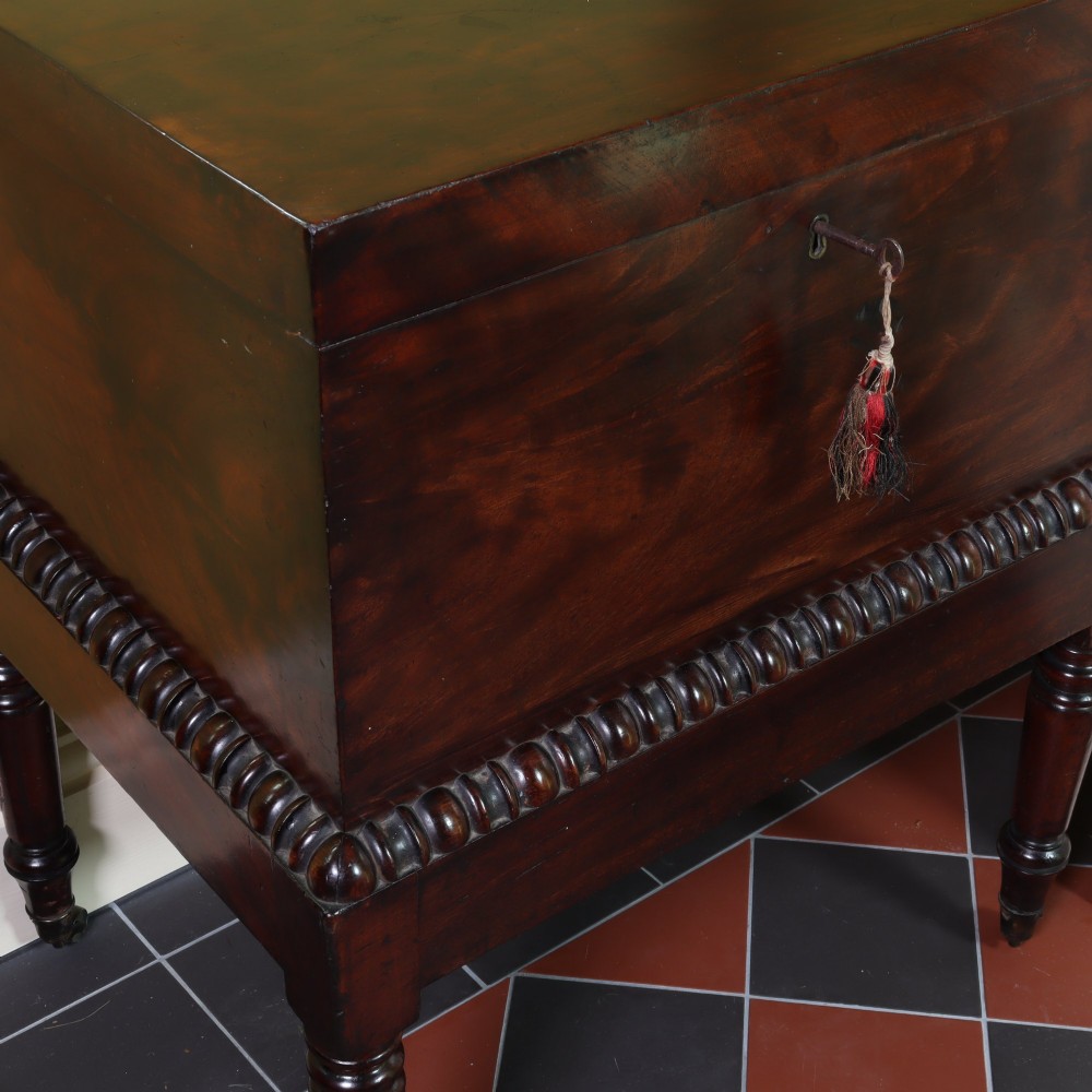 A Georgian flame mahogany rectangular cellarette chest on a stand featuring turned legs, gadrooned trim, and brass castors. View III