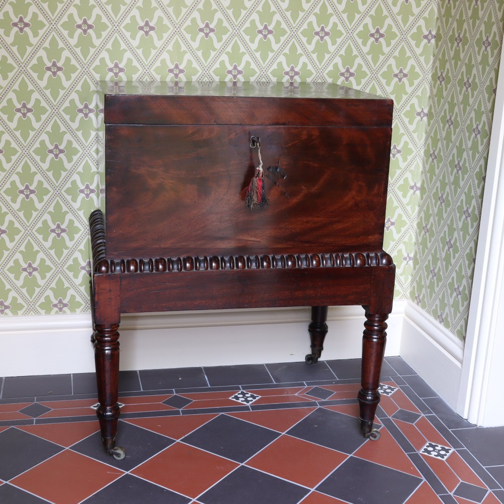 A Georgian flame mahogany rectangular cellarette chest on a stand featuring turned legs, gadrooned trim, and brass castors. View V
