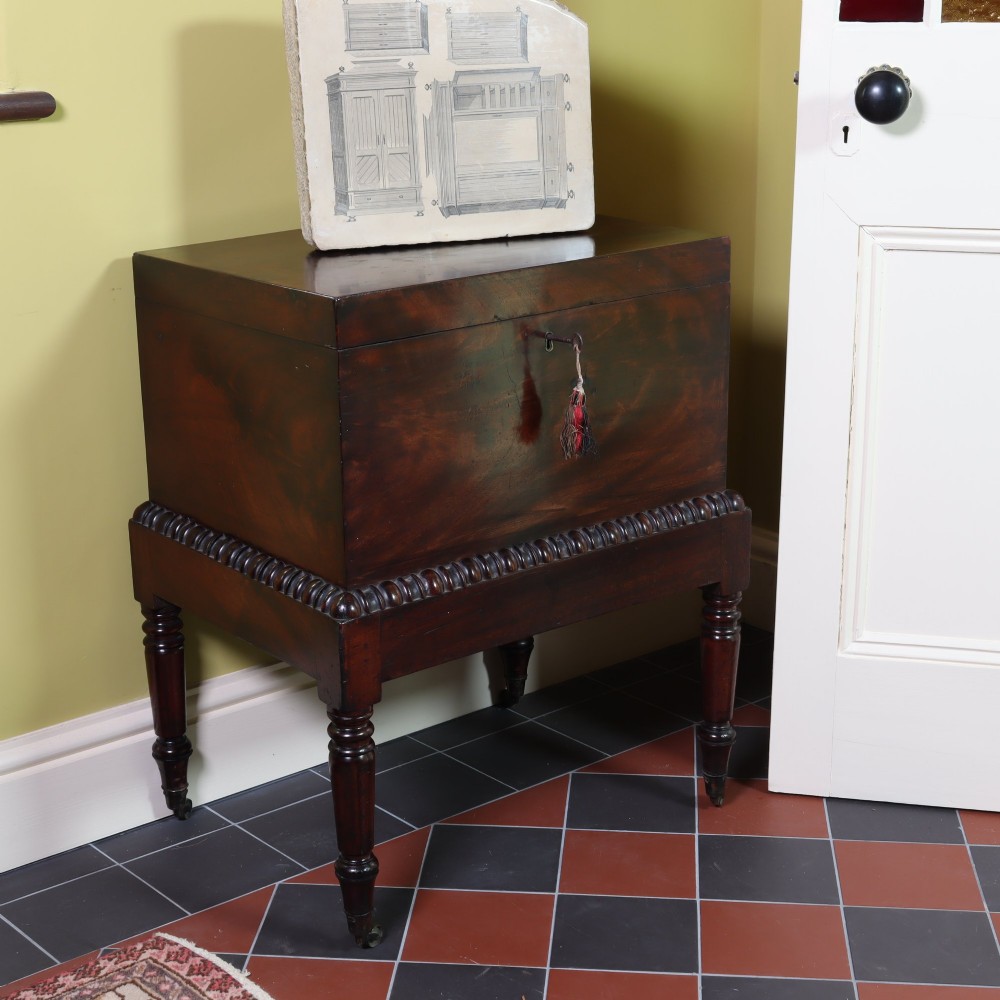A Georgian flame mahogany rectangular cellarette chest on a stand featuring turned legs, gadrooned trim, and brass castors. View VI