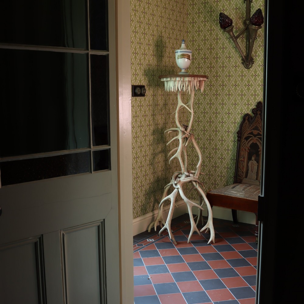 A tall, rustic torchiere stand constructed from intertwined natural deer antlers supporting an octagonal wooden top trimmed with downward-pointing antler tines. View II