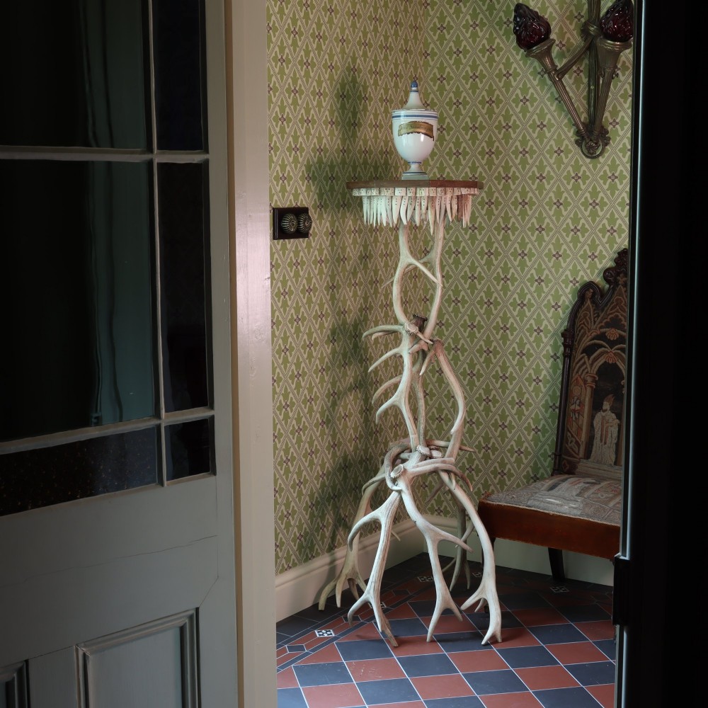 A tall, rustic torchiere stand constructed from intertwined natural deer antlers supporting an octagonal wooden top trimmed with downward-pointing antler tines. View III