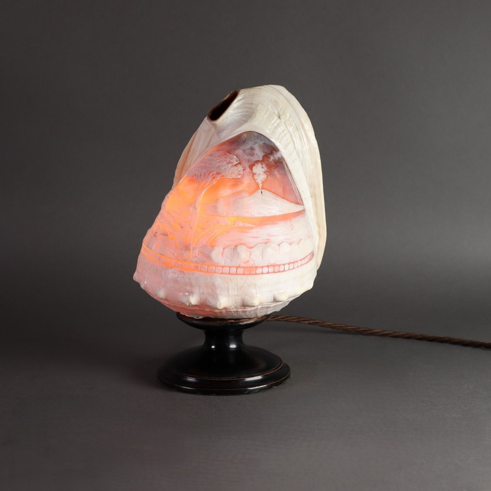 An illuminated 19th-century conch shell carved in relief with a scene depicting Mount Vesuvius, mounted on a turned ebonised wood base.