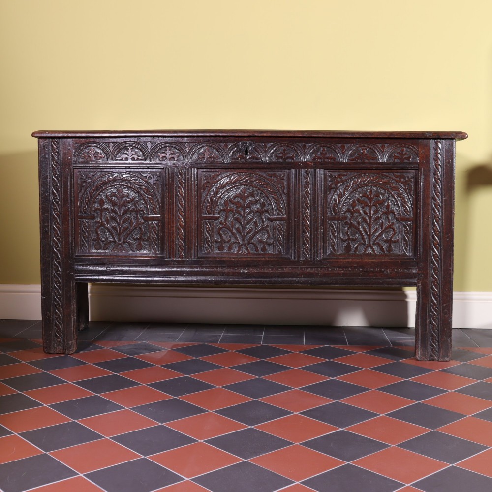 A mid-17th-century dark oak panelled coffer with three carved arch panels and a detailed frieze.