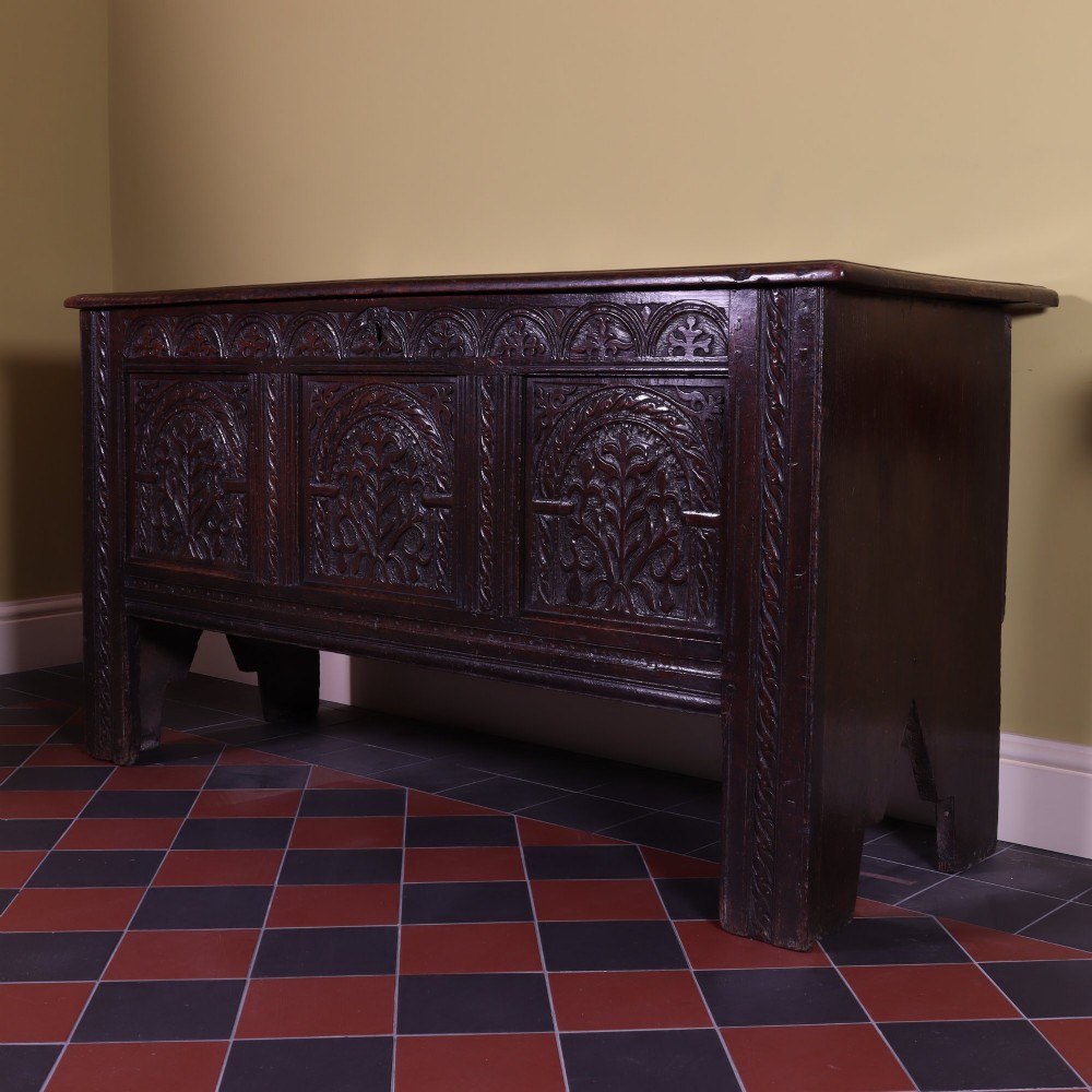 A mid-17th-century dark oak panelled coffer with three carved arch panels and a detailed frieze. View II