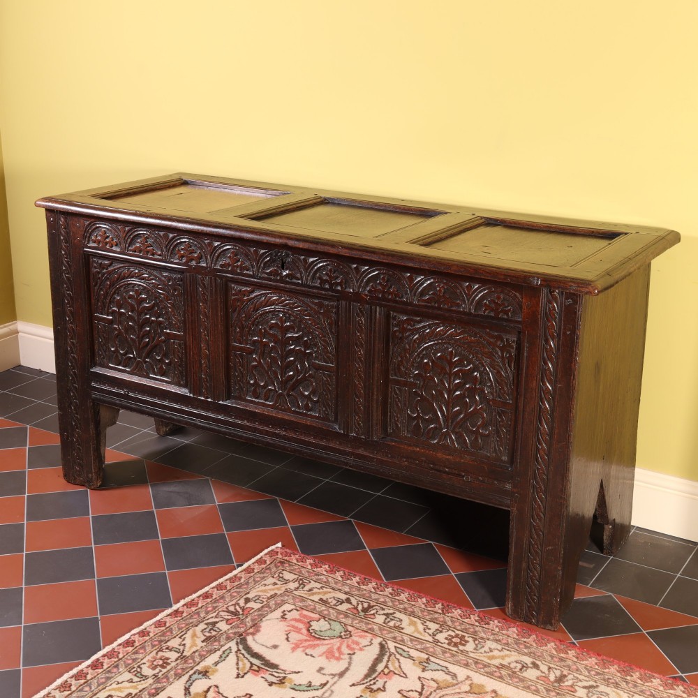 A mid-17th-century dark oak panelled coffer with three carved arch panels and a detailed frieze. View III
