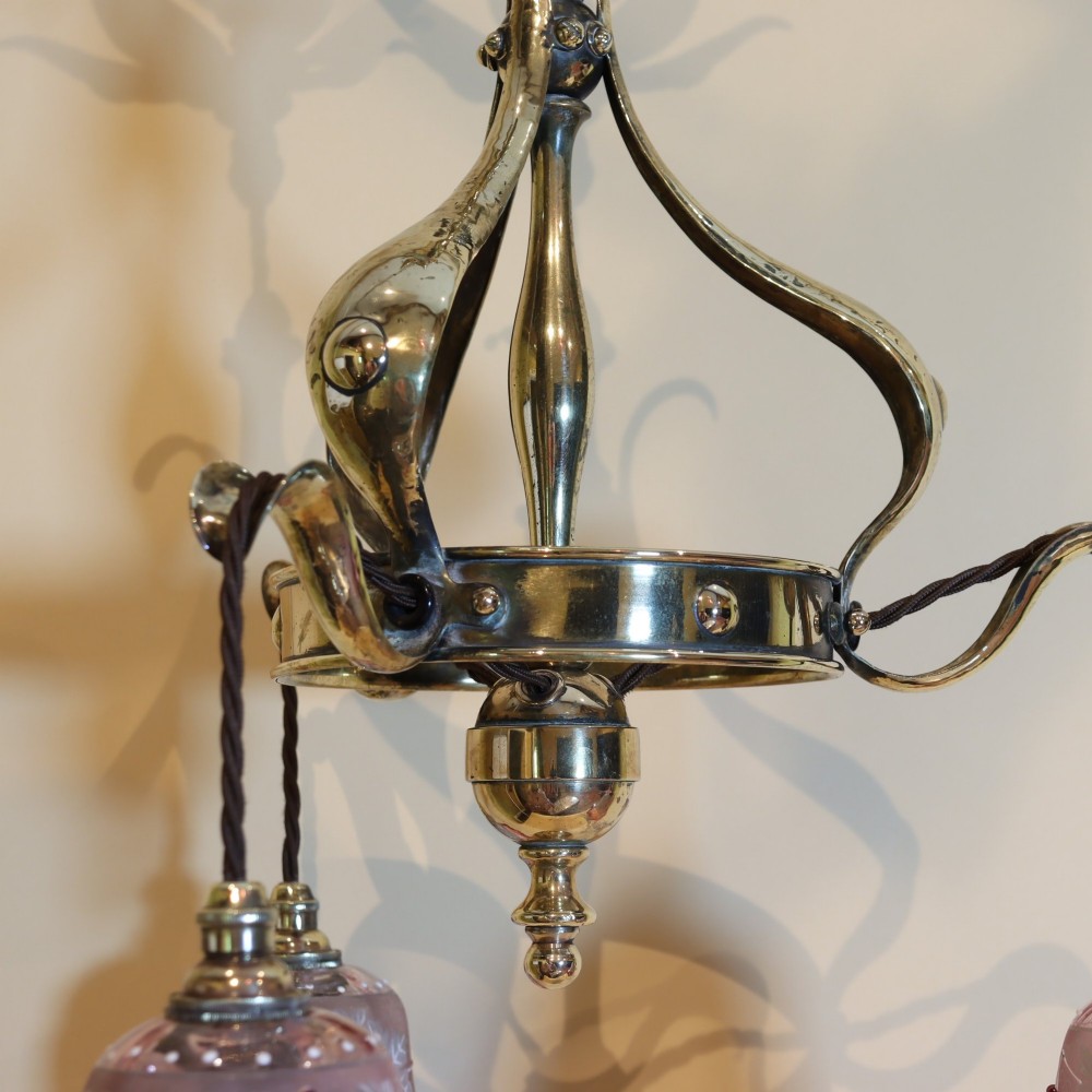 An Arts and Crafts brass ceiling light featuring three curved arms holding ruffled cranberry glass shades with painted floral motifs. View IV