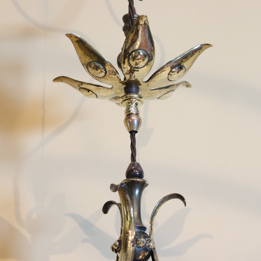 An Arts and Crafts brass ceiling light featuring three curved arms holding ruffled cranberry glass shades with painted floral motifs. View VI