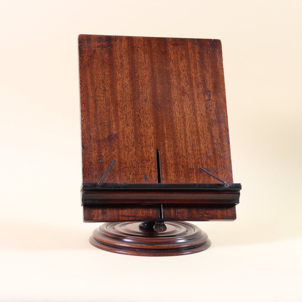 A 19th-century dark mahogany desktop reading stand featuring an upright wooden backplate, metal page retainers, and a moulded circular swivel base.