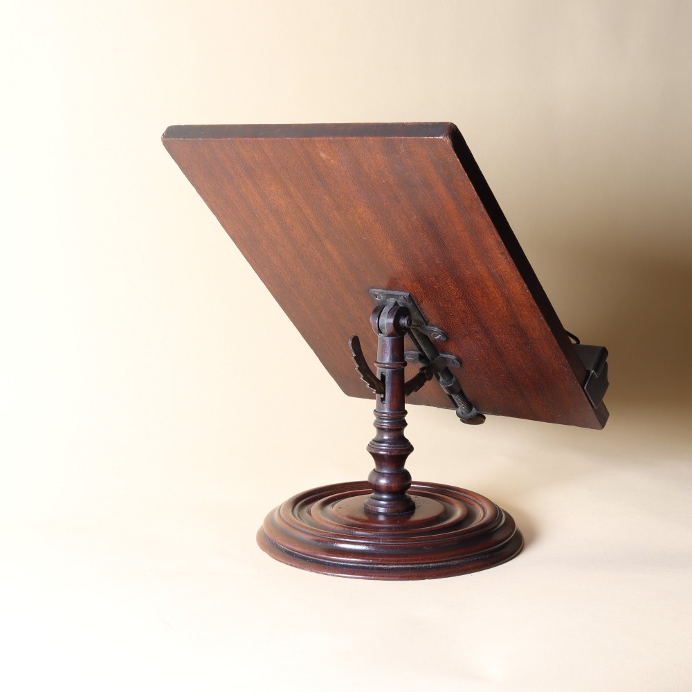 A 19th-century dark mahogany desktop reading stand featuring an upright wooden backplate, metal page retainers, and a moulded circular swivel base. View II