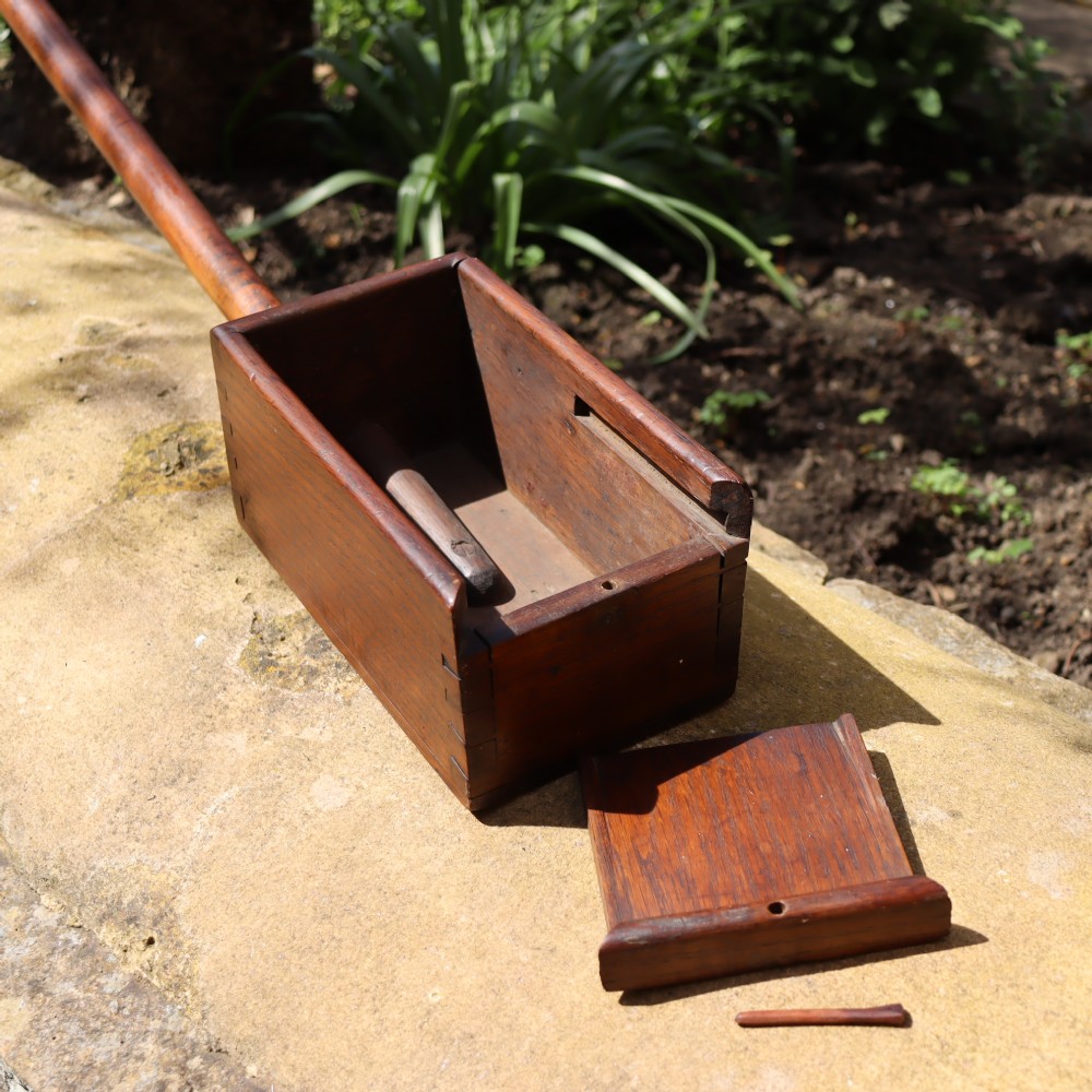An antique long-handled dark wooden church collection box with a turned pole and a rectangular open container at the end. View V
