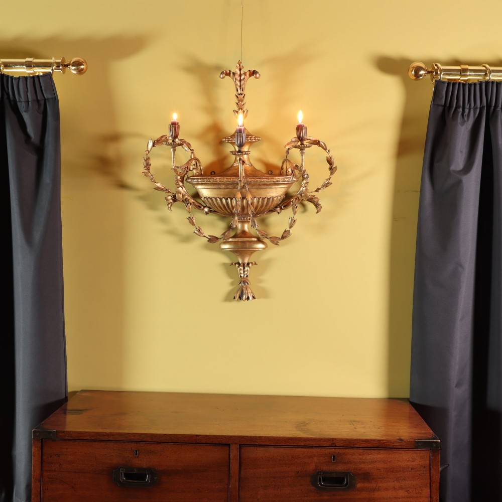 A George III style carved giltwood three-branch wall sconce featuring a central fluted urn motif flanked by scrolling foliate arms. View II