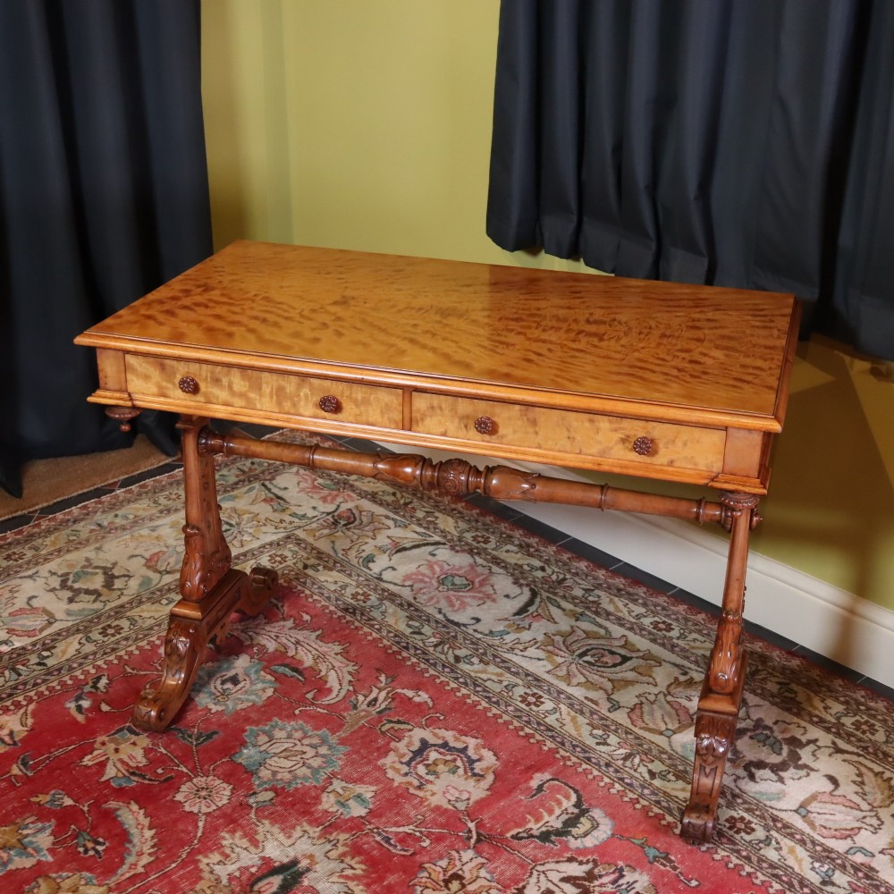 A Victorian satinwood side table featuring two frieze drawers with small round knobs, supported by carved trestle ends connected by a turned stretcher. View II