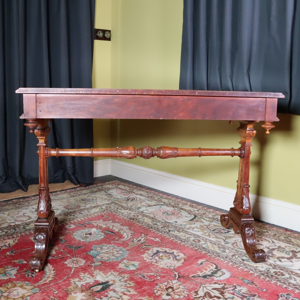 A Victorian satinwood side table featuring two frieze drawers with small round knobs, supported by carved trestle ends connected by a turned stretcher. View VI