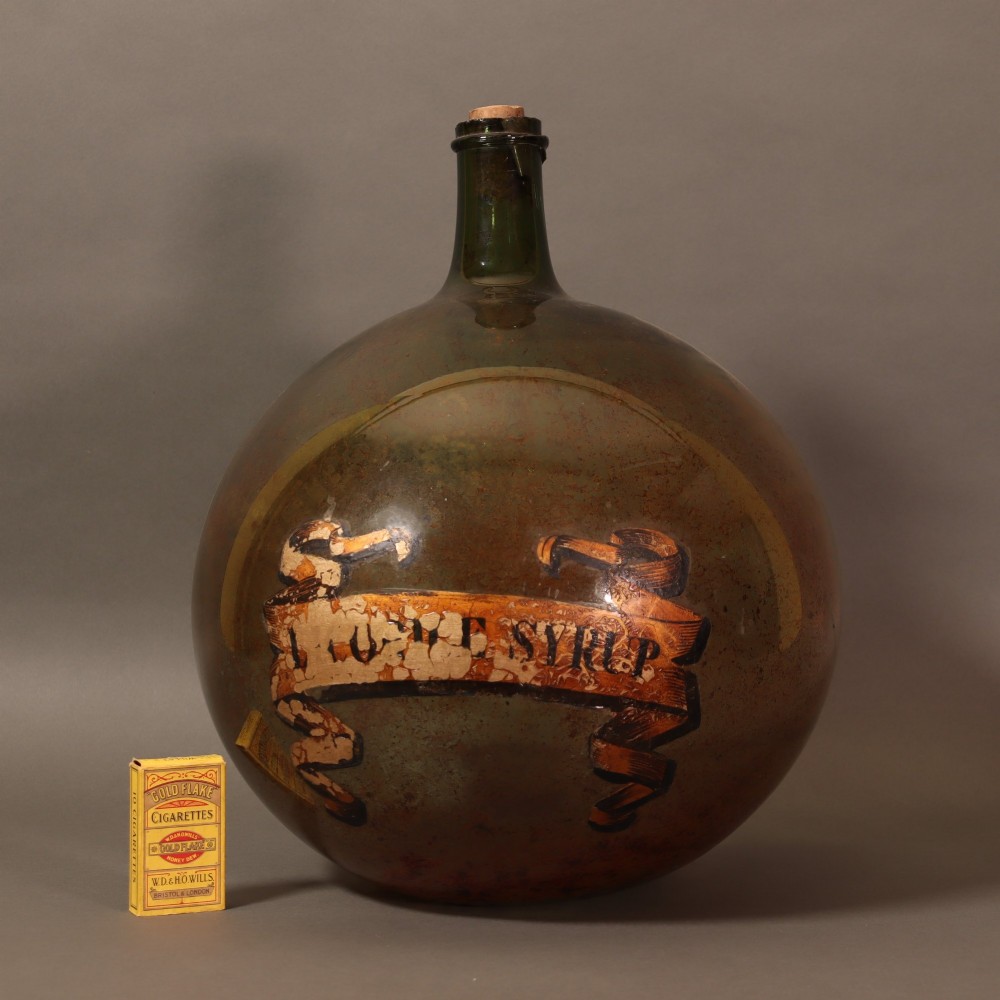 A large spherical olive green glass apothecary carboy featuring a painted banner with gilded scroll lettering. View VII