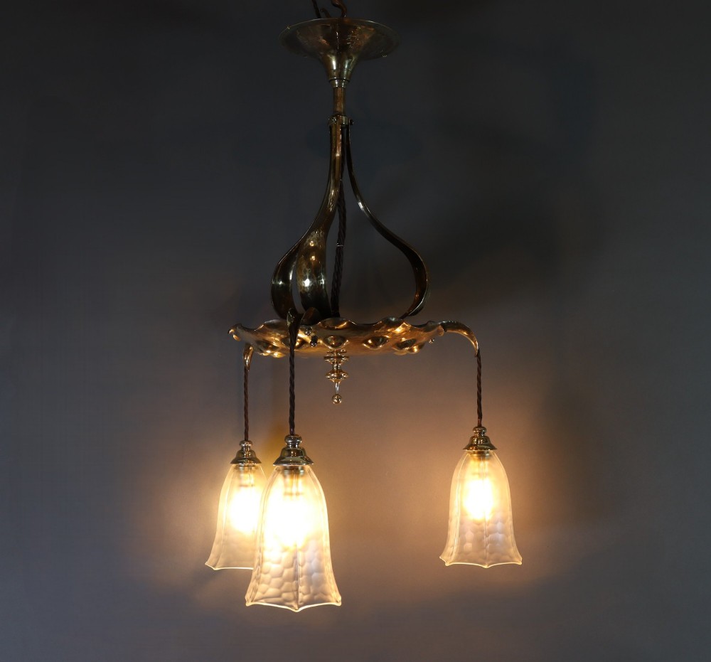 An antique Arts and Crafts brass ceiling fixture featuring a central hand-hammered canopy and three suspended drop pendant lights with frosted bell glass shades. View II