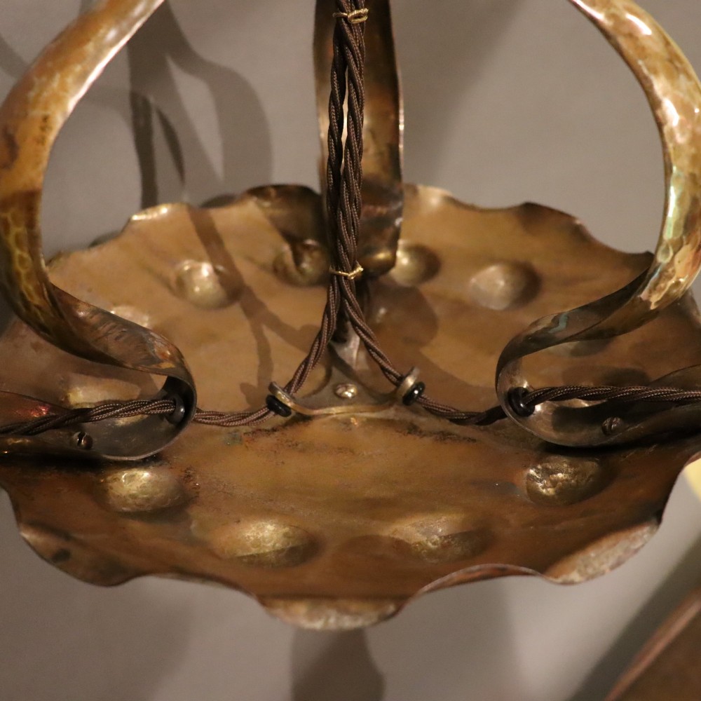 An antique Arts and Crafts brass ceiling fixture featuring a central hand-hammered canopy and three suspended drop pendant lights with frosted bell glass shades. View V