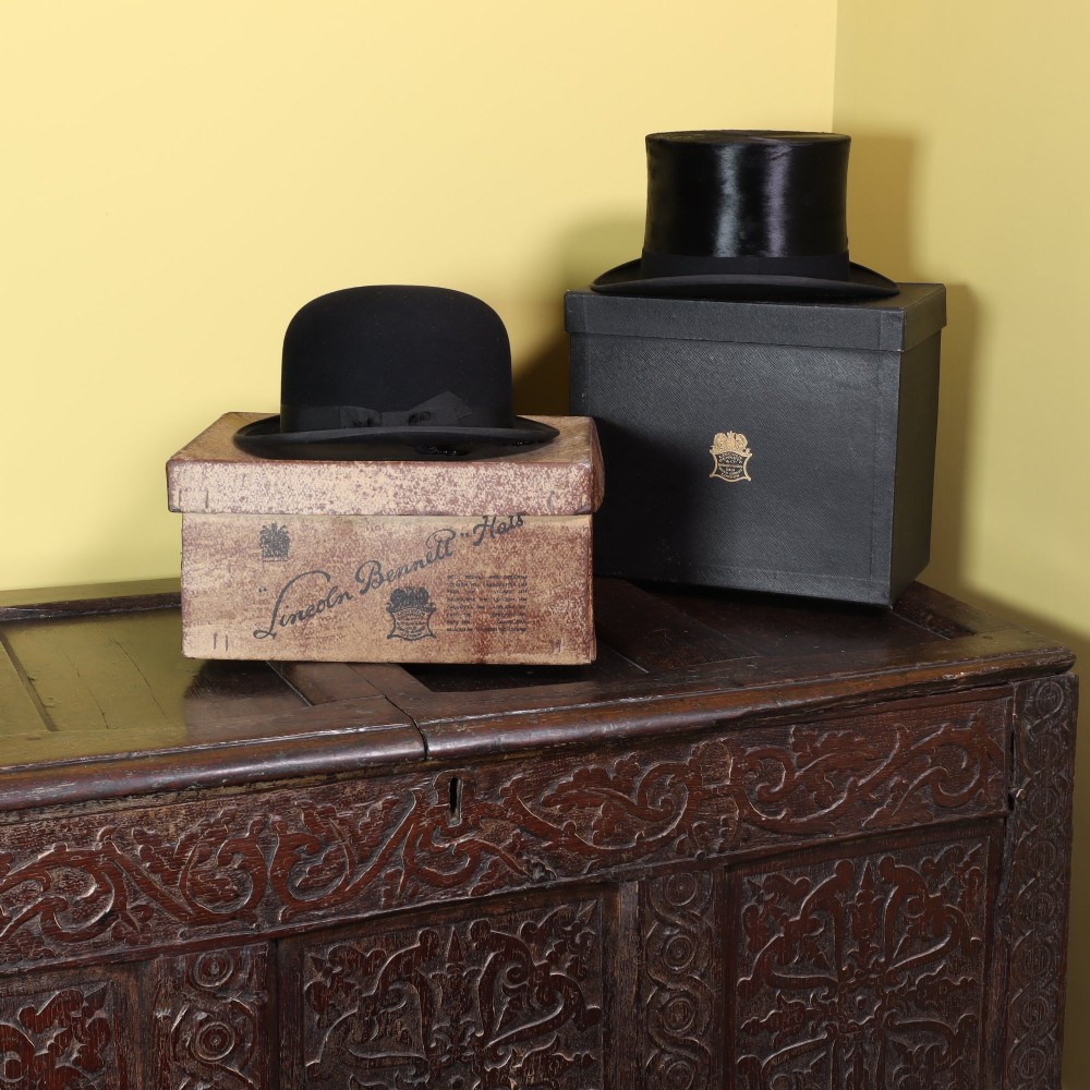 A black silk top hat resting on stacked fitted hat boxes beside a black bowler hat by Lincoln Bennett of London. View III