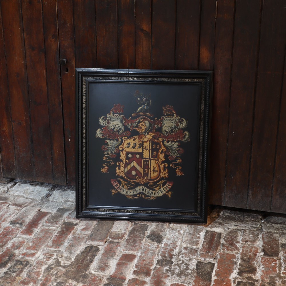 A large black-framed 19th-century panel featuring a painted coat of arms with red and cream mantling above a heraldic motto scroll.
