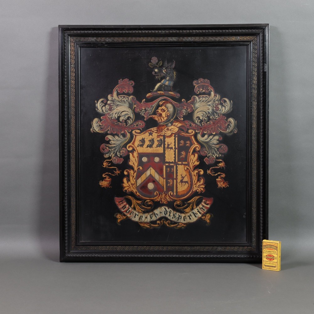 A large black-framed 19th-century panel featuring a painted coat of arms with red and cream mantling above a heraldic motto scroll. View III
