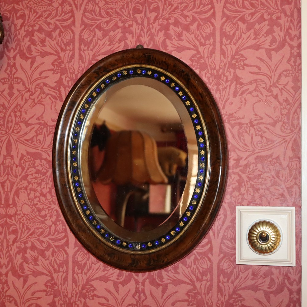 A late 19th-century oval wall mirror featuring a figured wood frame with an inner border of blue glass cabochons and gold star accents. View II