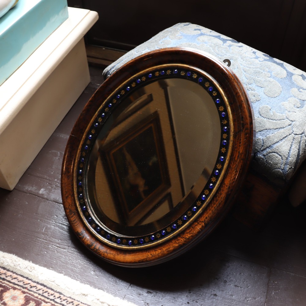 A late 19th-century oval wall mirror featuring a figured wood frame with an inner border of blue glass cabochons and gold star accents. View IV