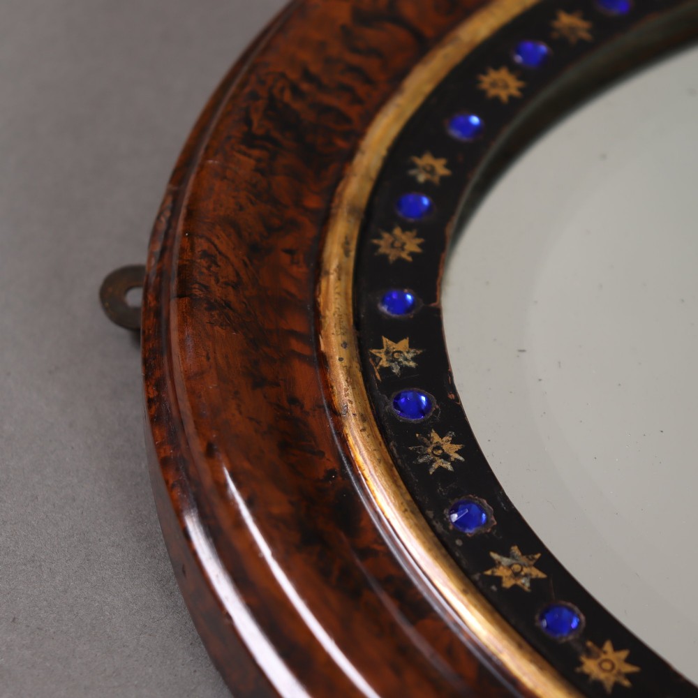 A late 19th-century oval wall mirror featuring a figured wood frame with an inner border of blue glass cabochons and gold star accents. View V
