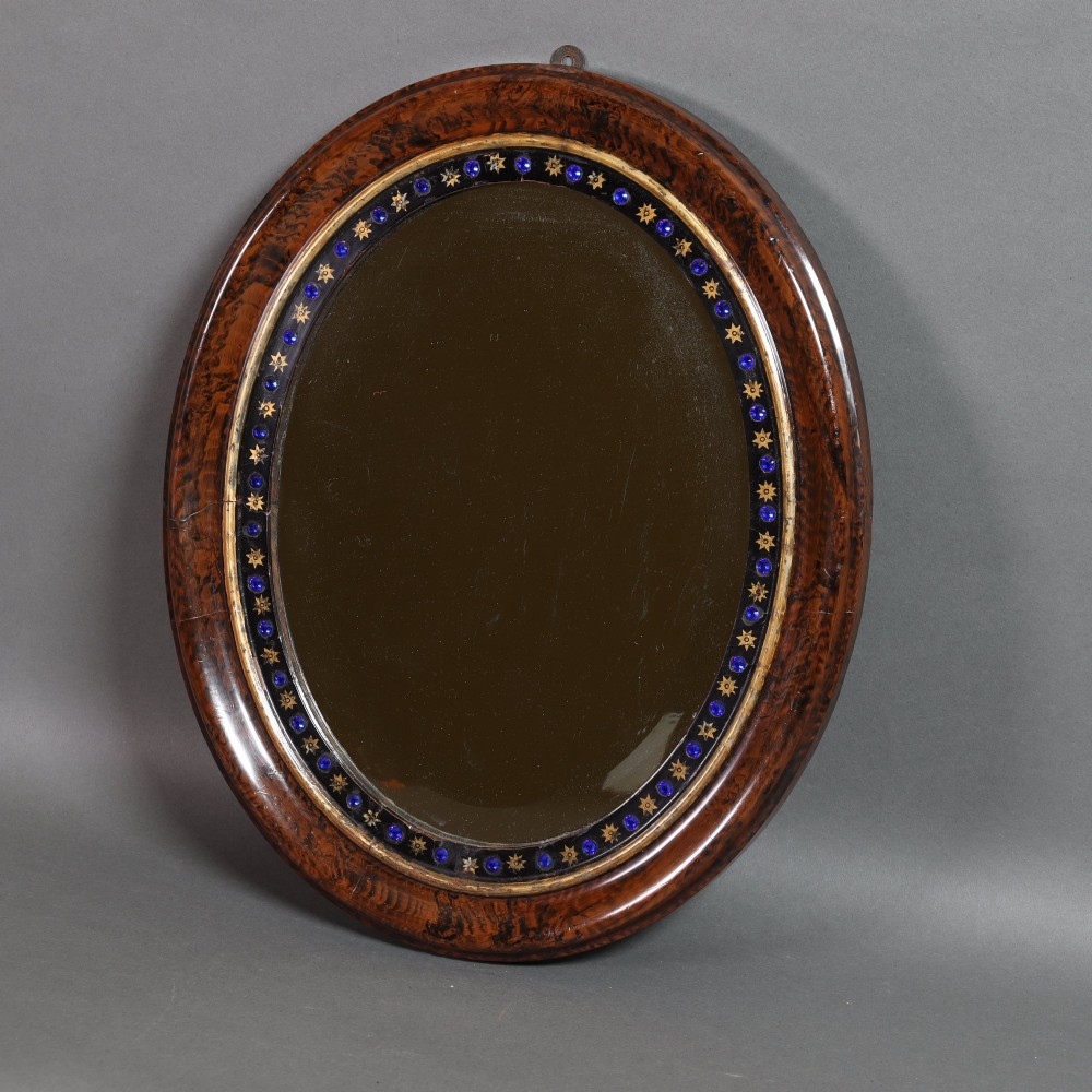 A late 19th-century oval wall mirror featuring a figured wood frame with an inner border of blue glass cabochons and gold star accents.