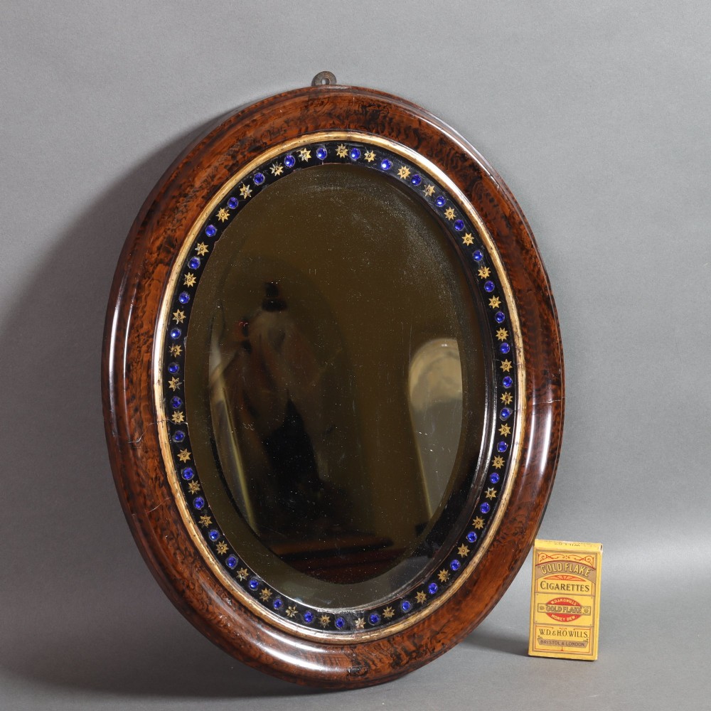 A late 19th-century oval wall mirror featuring a figured wood frame with an inner border of blue glass cabochons and gold star accents. View VI
