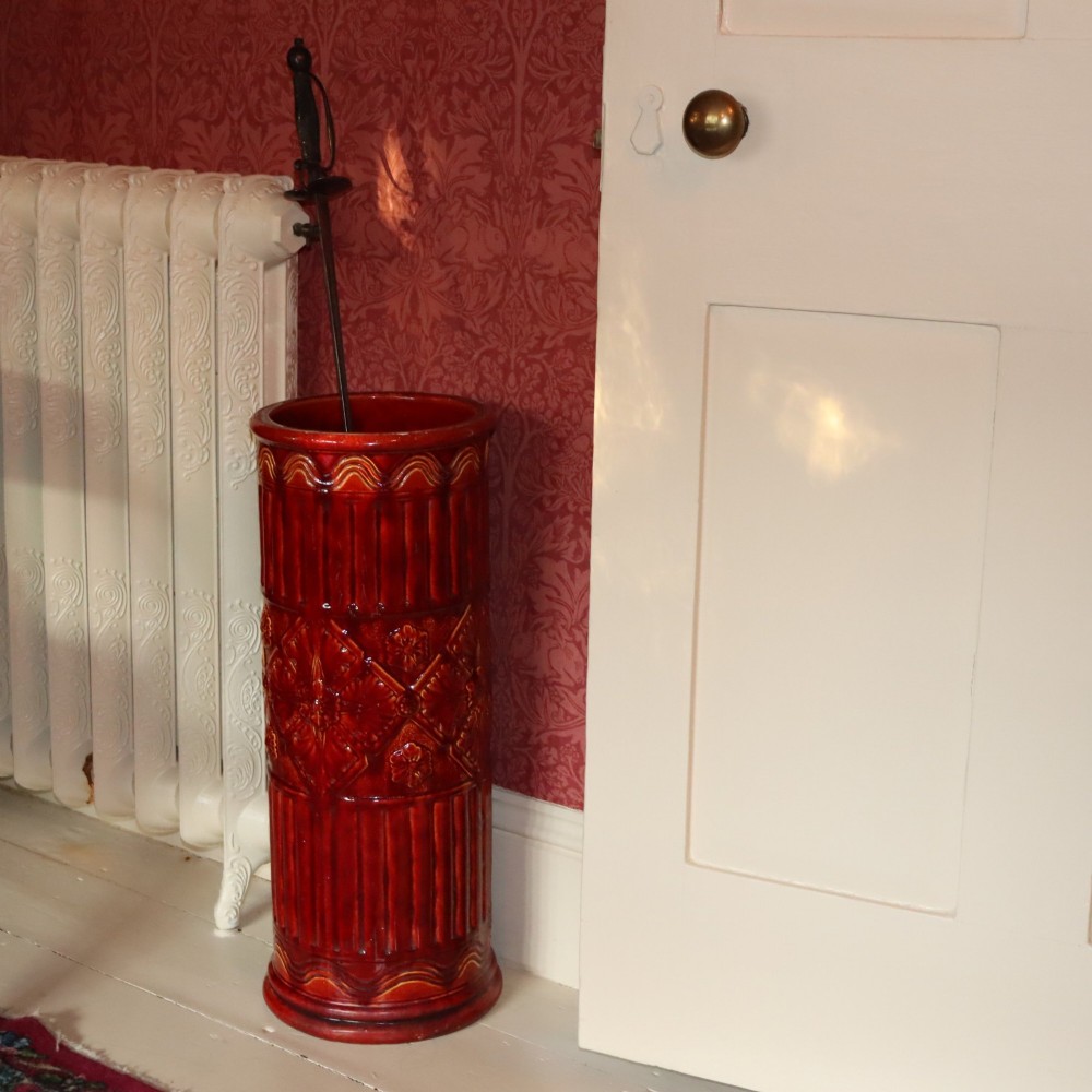 A tall cylindrical Victorian Burmantofts faience ceramic stick stand with a rich red glaze and intricate relief-moulded floral and geometric motifs. View II