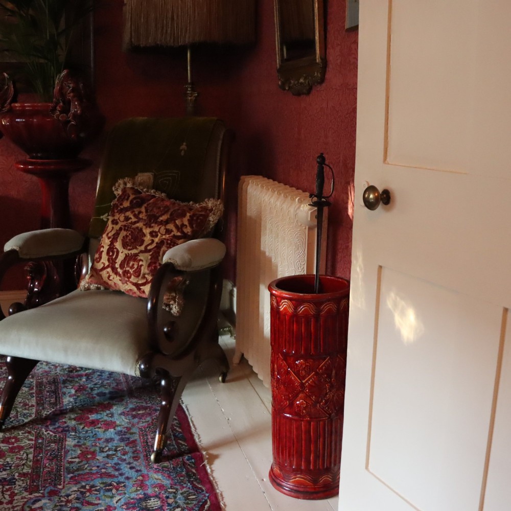 A tall cylindrical Victorian Burmantofts faience ceramic stick stand with a rich red glaze and intricate relief-moulded floral and geometric motifs. View III