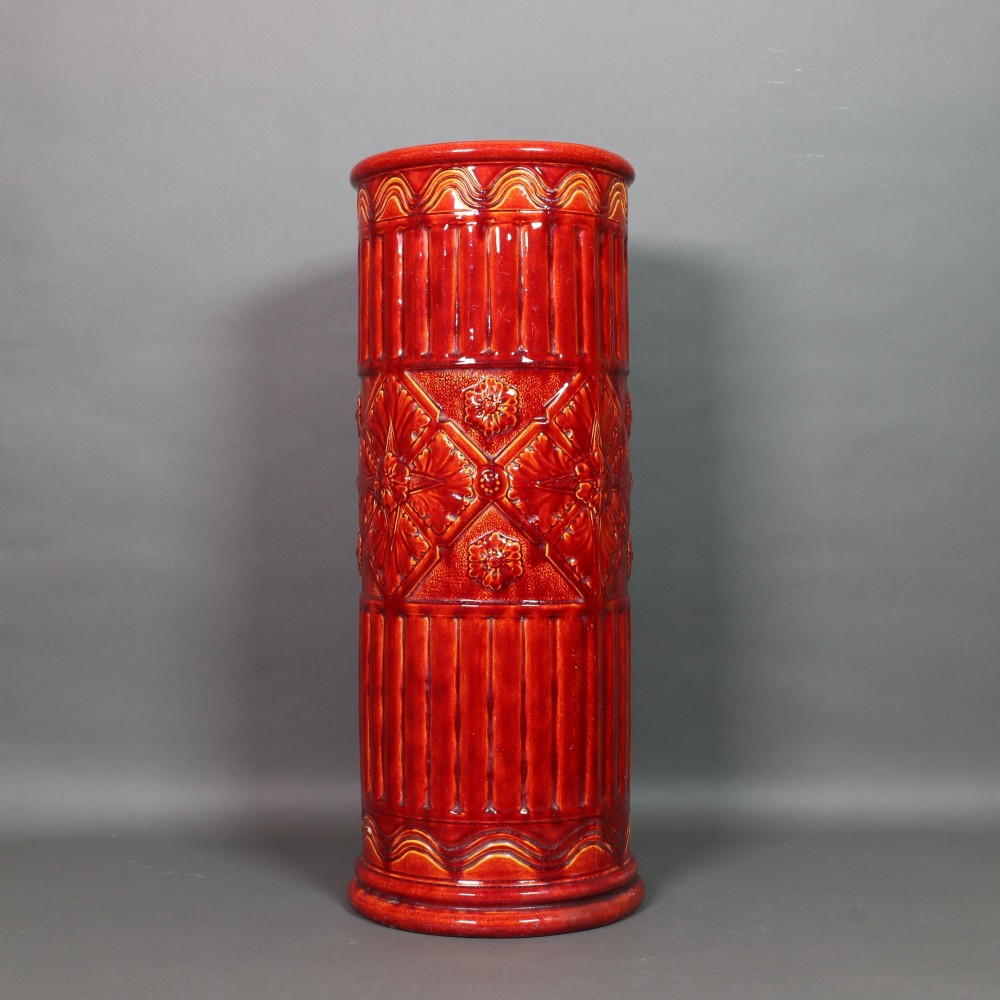 A tall cylindrical Victorian Burmantofts faience ceramic stick stand with a rich red glaze and intricate relief-moulded floral and geometric motifs.