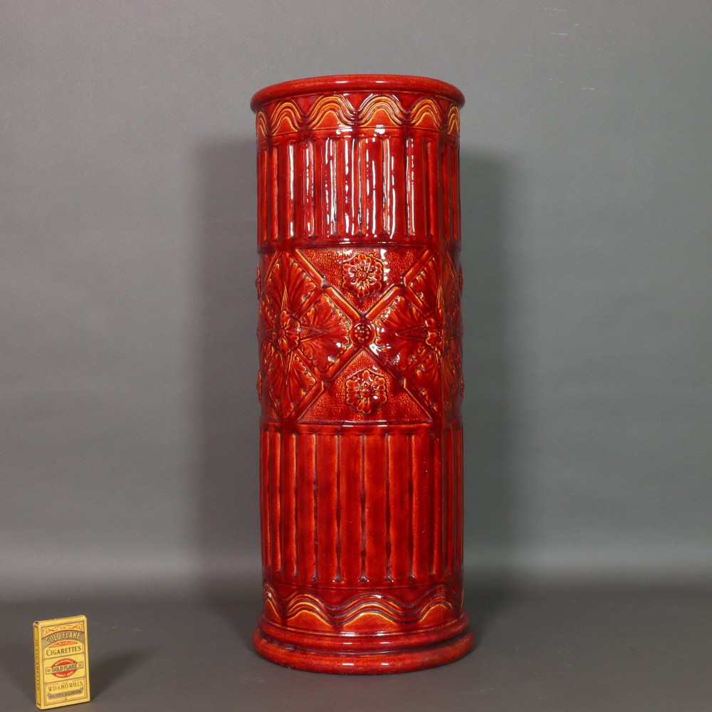 A tall cylindrical Victorian Burmantofts faience ceramic stick stand with a rich red glaze and intricate relief-moulded floral and geometric motifs. View IV