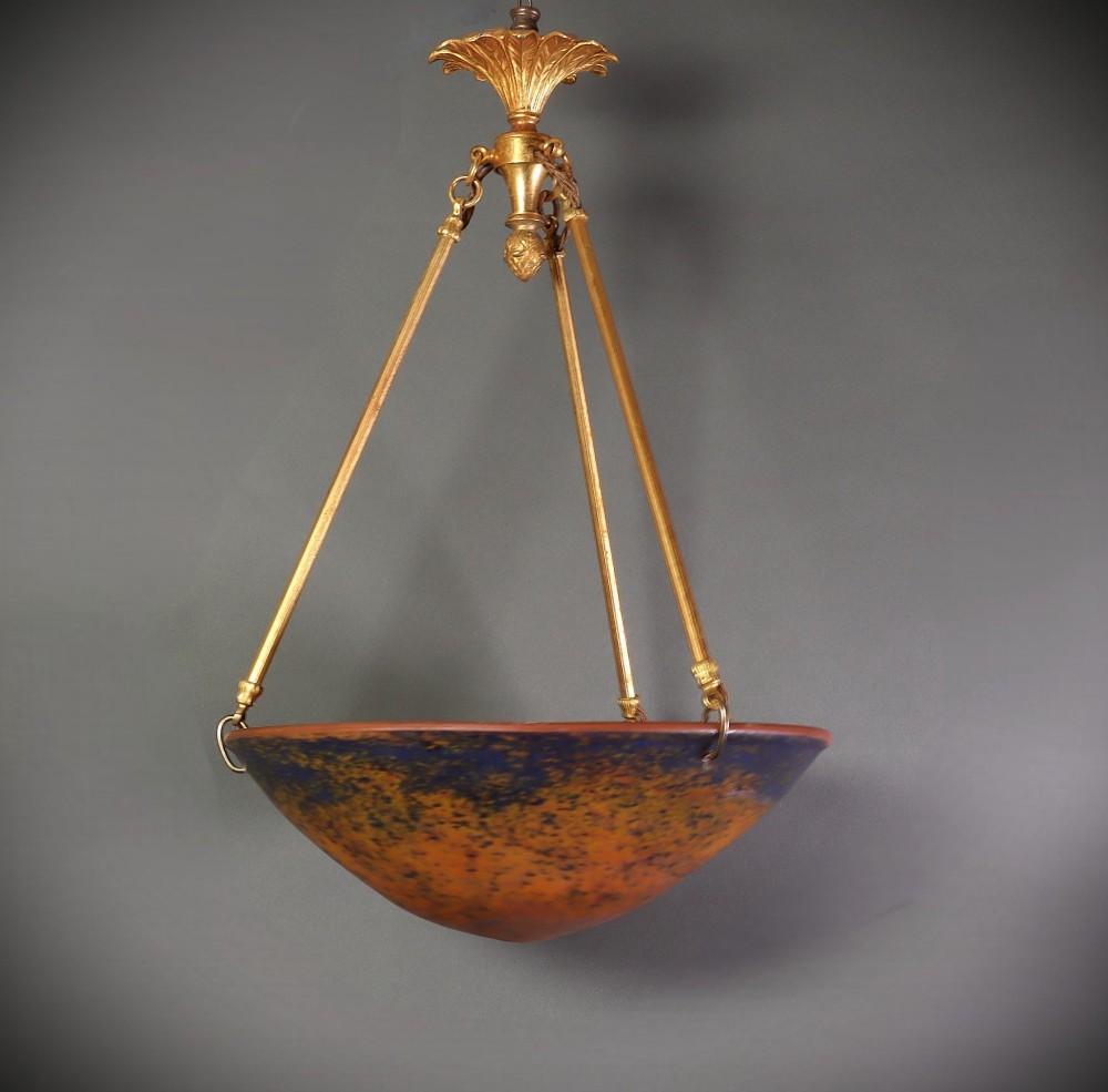 An Art Deco glass plafonnier featuring a warm mottled orange and dark blue bowl shade suspended by three gilt metal rods and a decorative ceiling rose. View II
