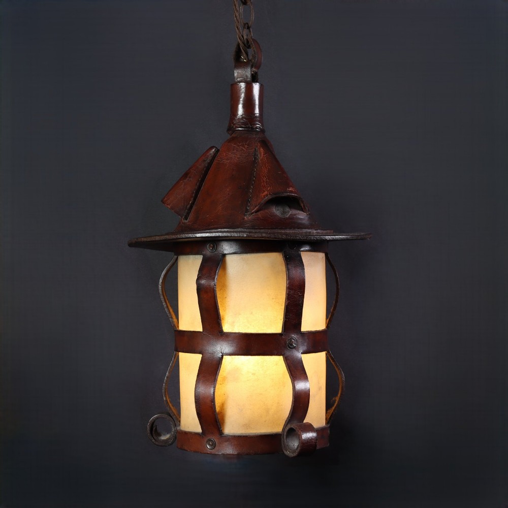 An Arts and Crafts hanging lantern featuring a hand-stitched dark brown leather framework surrounding illuminated vellum panels with scrolled metal feet.