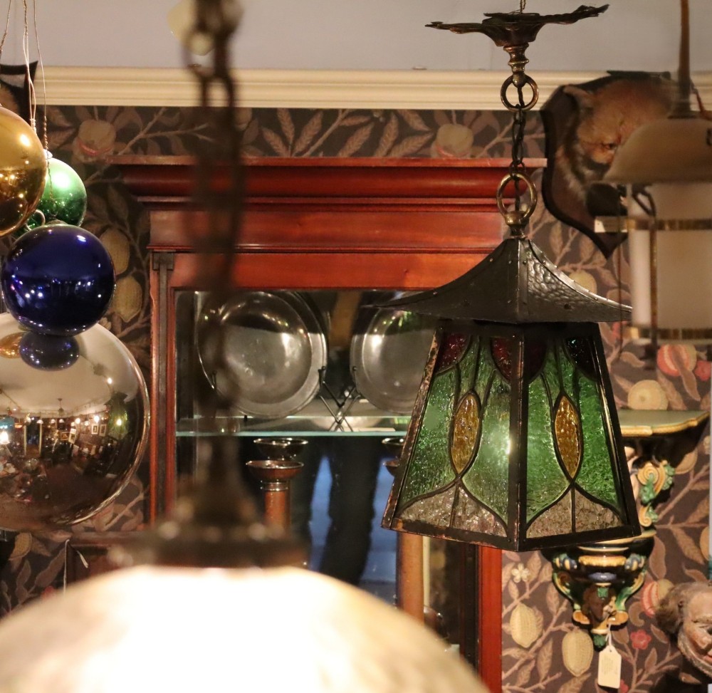 An Arts and Crafts planished copper hanging lantern featuring leaded green, yellow, and clear glass panels suspended from a chain and floral ceiling rose. View II